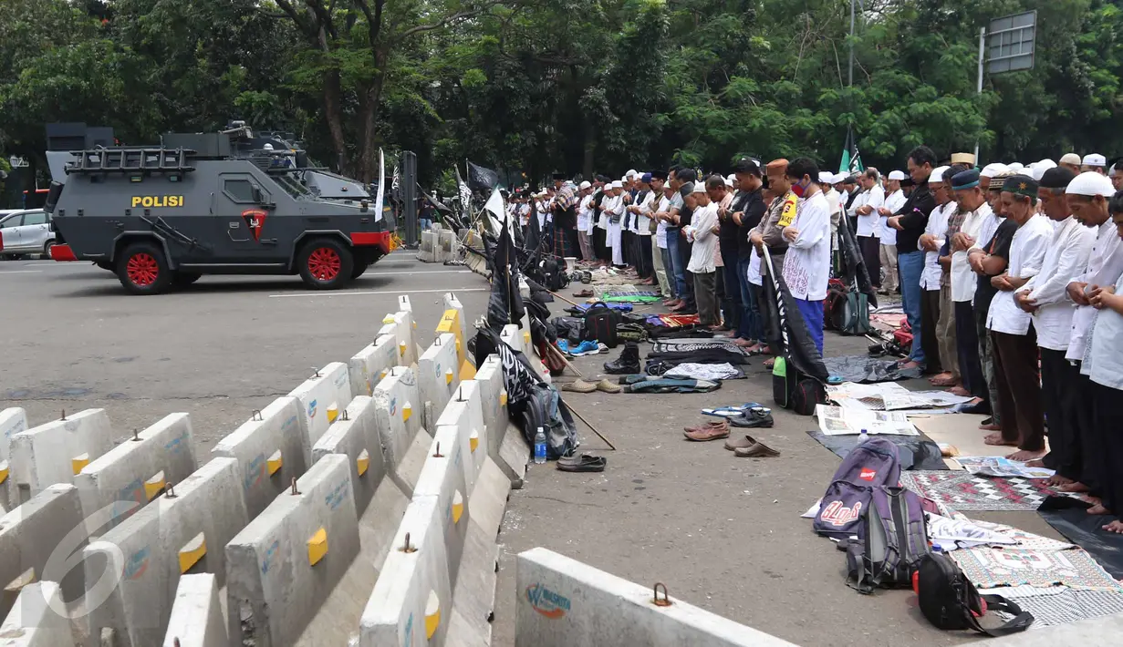 Massa aksi damai 4 November melaksanakan salat Jumat di Jalan Merdeka Barat, Jakarta, Jumat (4/11). Mereka menggelar salat Jumat di belakang pembatas beton dan mobil barakuda yang mengamankan kawasan itu. (Liputan6.com/Faizal Fanani)