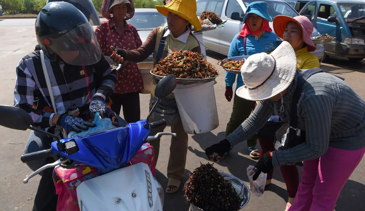 Pengendara motor membeli tarantula goreng yang dijajakan pedagang di wilayah Skun, Provinsi Kampong Cham, Kamboja, 4 Desember 2019. Daerah yang kerap dijuluki "Spiderville" tersebut menjadi tempat menarik bagi para turis berburu aping, camilan tradisional dari tarantula ini. (TANG CHHIN Sothy / AFP)