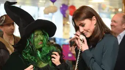 Seorang pekerja yang mengenakan kostum tampak mengamati Duchess of Cambridge, Kate Middleton yang tengah menggenggam gagang telepon saat menjadi broker dalam acara amal tahunan ICAP di London, Inggris, Rabu (9/12/2015). (AFP PHOTO/POOL/JEREMY Selwyn)