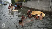 Sejumlah anak bermain di genangan air banjir di Kawasan Muara Angke, Jakarta, Rabu (11/1). Banjir ini juga telah merendam ratusan rumah, toko, dan tempat pengeringan ikan asin. (Liputan6.com/Gempur M. Surya)