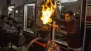 Ramadan Edwan, seorang tukang cukur asal Palestina, menggunakan api untuk mencukur rambut pelanggannya di sebuah barbershop di kamp pengungsian Rafah, di selatan Jalur Gaza, Rabu (1/2). (MAHMUD HAMS/AFP)