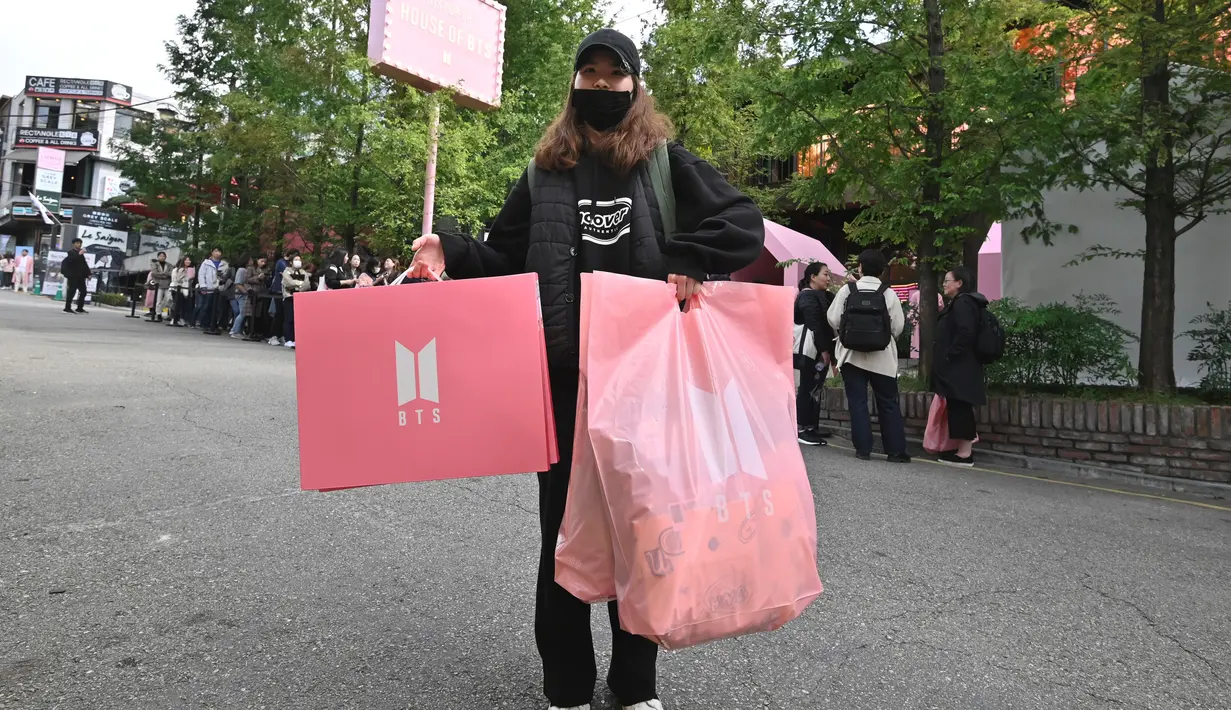 Penggemar membawa kantong plastik usai berbelanja dari toko pop-up BTS di Distrik Gangnam, Seoul, Korea Selatan, Jumat (18/10/2019). Ada sekitar 200 lebih jenis merchandise baru ditampilkan di ruang pamer. (Jung Yeon-je/AFP)