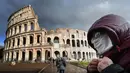 Seorang pria mengenakan masker pelindung melewati Colosseum di Roma, Italia, 7 Maret 2020. Hingga 21 Maret 2013, sebanyak 47.021 orang terinfeksi virus corona COVID-19 di Italia dengan korban meninggal mencapai 4.032 orang. (Photo by Alberto PIZZOLI/AFP)