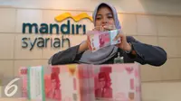 Petugas menghitung uang di Bank Mandiri Syariah, Jakarta, Kamis (14/7). Otoritas Jasa Keuangan (OJK) memastikan hanya bank syariah besar yang dilibatkan dalam pelaksanaan kebijakan pengampunan pajak. (Liputan6.com/Angga Yuniar)