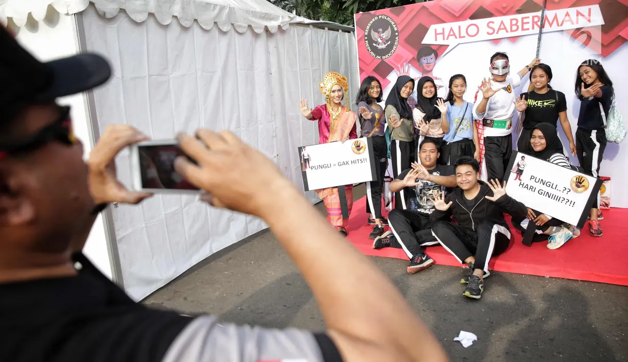 Satgas saber pungli mengenakan kostum super hero dan tradisional berfoto bersama dengan warga saat mensosialisasikan tolak pungli di Car Free Day, Jakarta, Minggu (12/11). (Liputan6.com/Faizal Fanani)
