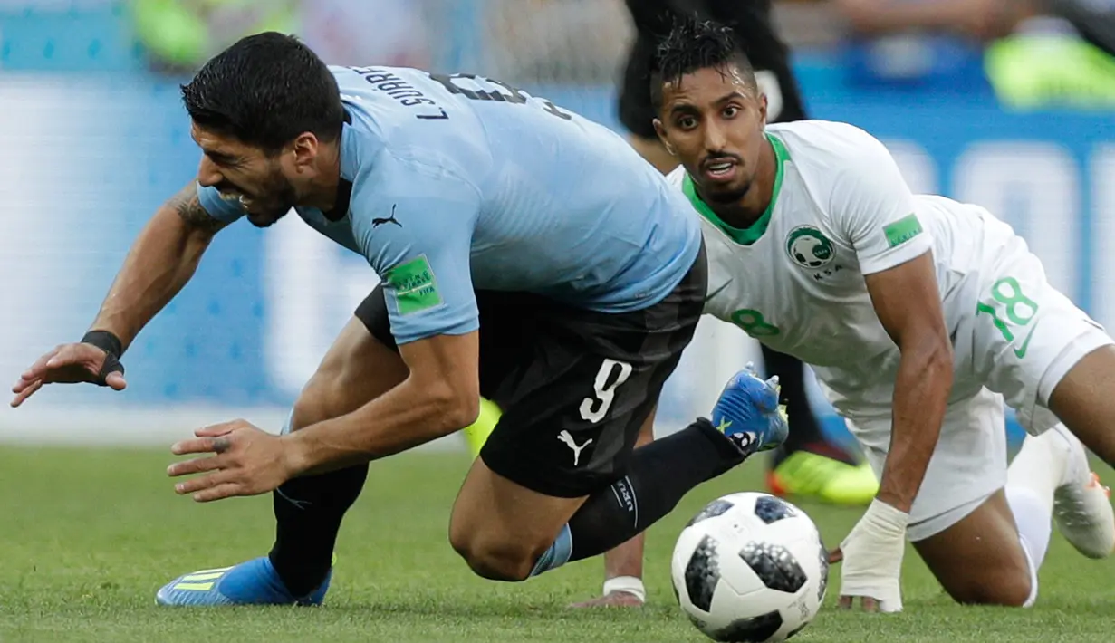 Penyerang Uruguay, Luis Suarez dan pemain Arab Saudi Salem Aldawsari terjatuh saat berebut bola pada pertandingan kedua Grup A Piala Dunia 2018 di Rostov Arena, Rabu (20/6). Uruguay mengalahkan Arab Saudi 1-0 berkat gol Suarez. (AP/Andrew Medichini)