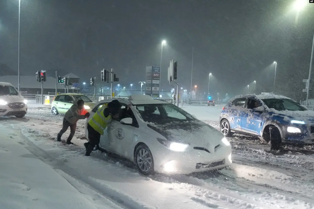 Sejumlah warga mendorong mobil yang terjebak di jalanan bersalju di Leeds, Inggris, pada 5 Januari 2025. (AP)