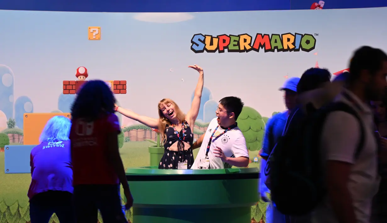 Pengunjung berpose di depan poster game Super Mario di booth Nintendo pada pameran video game Gamescom di Cologne, Jerman bagian barat, pada 23 Agustus 2023. (AFP/Ina Fassbeder)