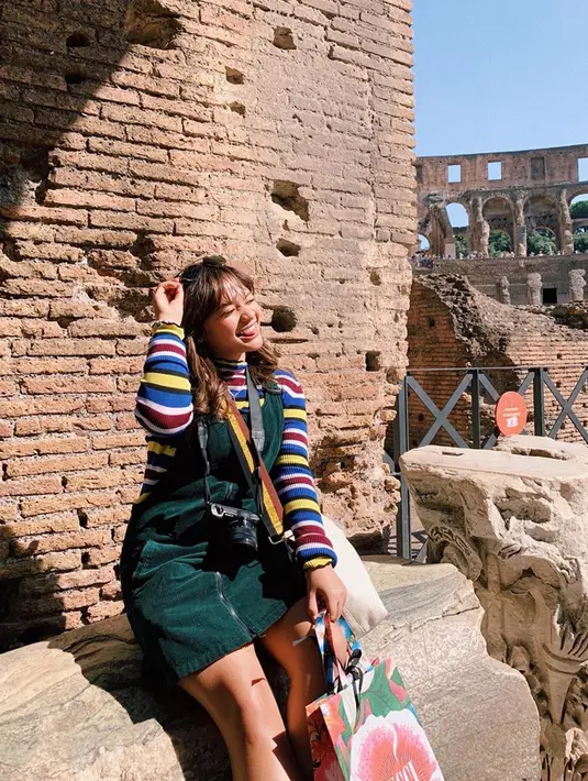 Gaya dan penampilan Amel Carla saat ini semakin dewasa. Amel Carla tengah berfoto sambil memegang kacamatanya dengan latar belakang di Colloseum, Roma. (Liputan6.com/IG/@amelcarla)