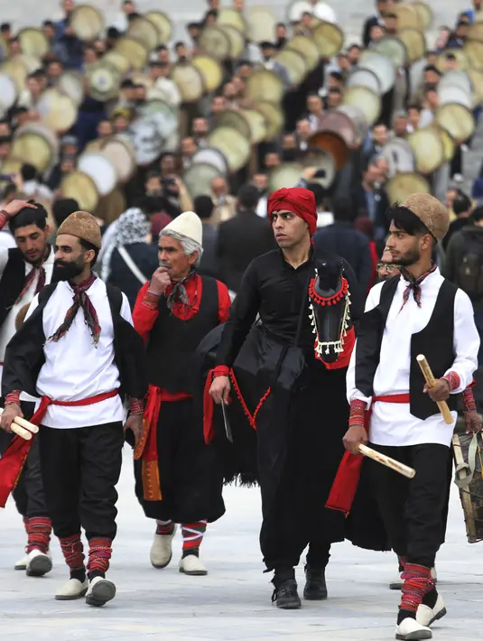 Sekelompok pemain cerita rakyat dari wilayah timur Iran berjalan saat musisi daerah Kurdi memainkan Daf, drum Persia genggam, dalam upacara menjelang Tahun Baru Iran, atau Nowruz, di sebuah taman di Teheran, Iran (14/3/2022). Nowruz akan diselenggarakan pada 20 Maret. (AP Photo/Vahid Salemi)