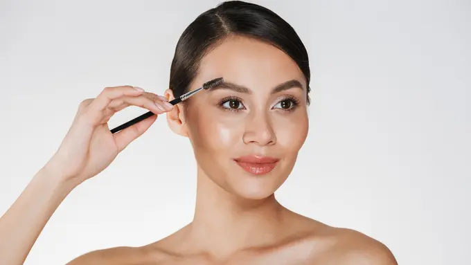 Seorang perempuan sedang merapikan alisnya menggunakan brush make up (Foto Dok: Freepik/ drobotdean)