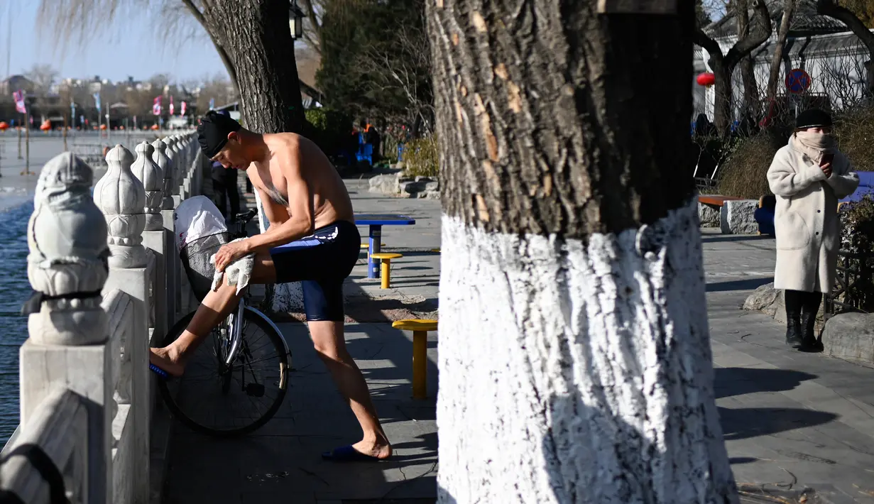 Seorang pria menyeka tubuhnya setelah berenang di sebuah danau yang airnya sebagian membeku di Beijing pada Senin (30/12/2019). Penduduk lokal banyak menggemari kebiasaan berenang di musim dingin dimana banyak sungai dan danau-danau mulai membeku. (WANG ZHAO / AFP)