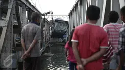 Warga mengamati evakuasi bus TransJakarta yang terperosok ke sungai usai ditabrak kereta api Senja Utama Solo di perlintasan kereta Mangga Dua, Jakarta, Kamis (19/5). Sopir mobil Avanza dan TransJakarta mengalami luka-luka. (Liputan6.com/Faizal Fanani)