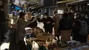 Seorang penjual (kiri) berbicara kepada seorang wanita saat orang-orang berjalan melalui jalan di area "pasar ikan luar" Tsukiji di Tokyo pada 28 Desember 2022. Menjelang liburan Tahun Bar, turis asing dan penduduk lokal berkunjung  ke pasar itu untuk menikmati hidangan bermacam makanan laut. (AFP/Richard A. Brooks)