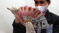 Karyawan menunjukkan uang rupiah dan dolar AS di Jakarta, Rabu (30/12/2020). Nilai tukar rupiah di pasar spot ditutup menguat 80 poin atau 0,57 persen ke level Rp 14.050 per dolar AS. (Liputan6.com/Johan Tallo)