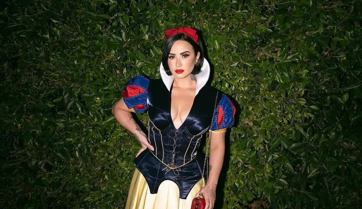 Demi Lovato hadir dengan karakter Putri Salju yang ikonik. Mengenakan atasan velvet navy dengan lengan balon dan rok kuningnya. Lengkap mengenakan bando merah. [@ddlovato]