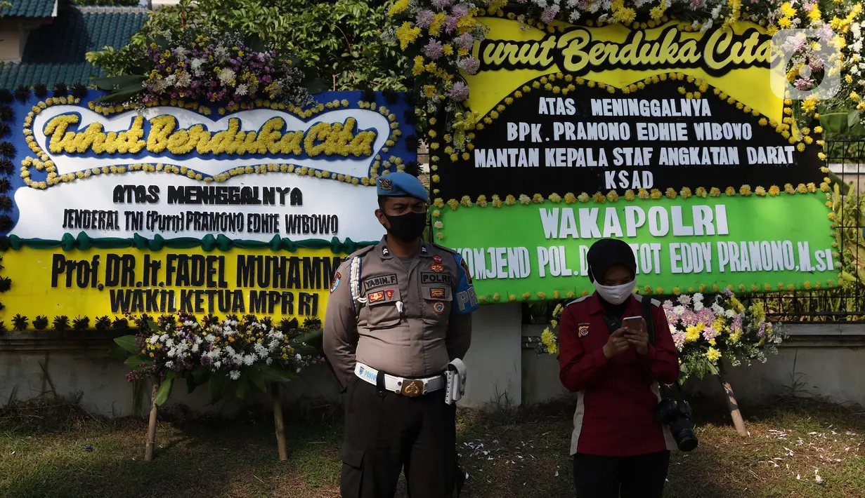 Personel Polri berada di depan karangan bunga tanda duka cita atas meninggalnya mantan KSAD Jenderal TNI (Purn) Pramono Edhie Wibowo di kawasan Puri Cikeas, Kab Bogor, Jabar, Minggu (14/6/2020). Pramono Edhie Wibowo wafat di usia 65 tahun akibat serangan jantung. (Liputan6.com/Helmi Fithriansyah)
