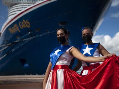 Ivanelis Jimenez (depan) dan Veronica Barreto mengenakan gaun bendera Puerto Rico saat menyambut penumpang kapal pesiar Mardi Gras Carnival yang berlabuh di Teluk San Juan, Puerto Rico, Selasa (3/8/2021). (AP Photo/Carlos Giusti)