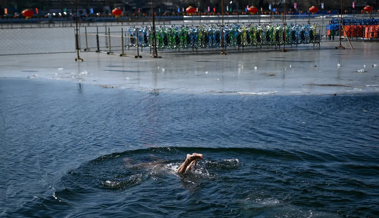 Seorang pria berenang di sebuah danau yang airnya sebagian membeku di Beijing pada Senin (30/12/2019). Penduduk lokal banyak menggemari kebiasaan berenang di musim dingin dimana banyak sungai dan danau-danau mulai membeku. (WANG ZHAO / AFP)