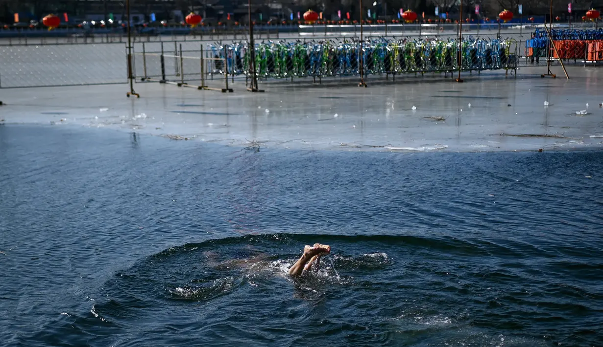 Seorang pria berenang di sebuah danau yang airnya sebagian membeku di Beijing pada Senin (30/12/2019). Penduduk lokal banyak menggemari kebiasaan berenang di musim dingin dimana banyak sungai dan danau-danau mulai membeku. (WANG ZHAO / AFP)