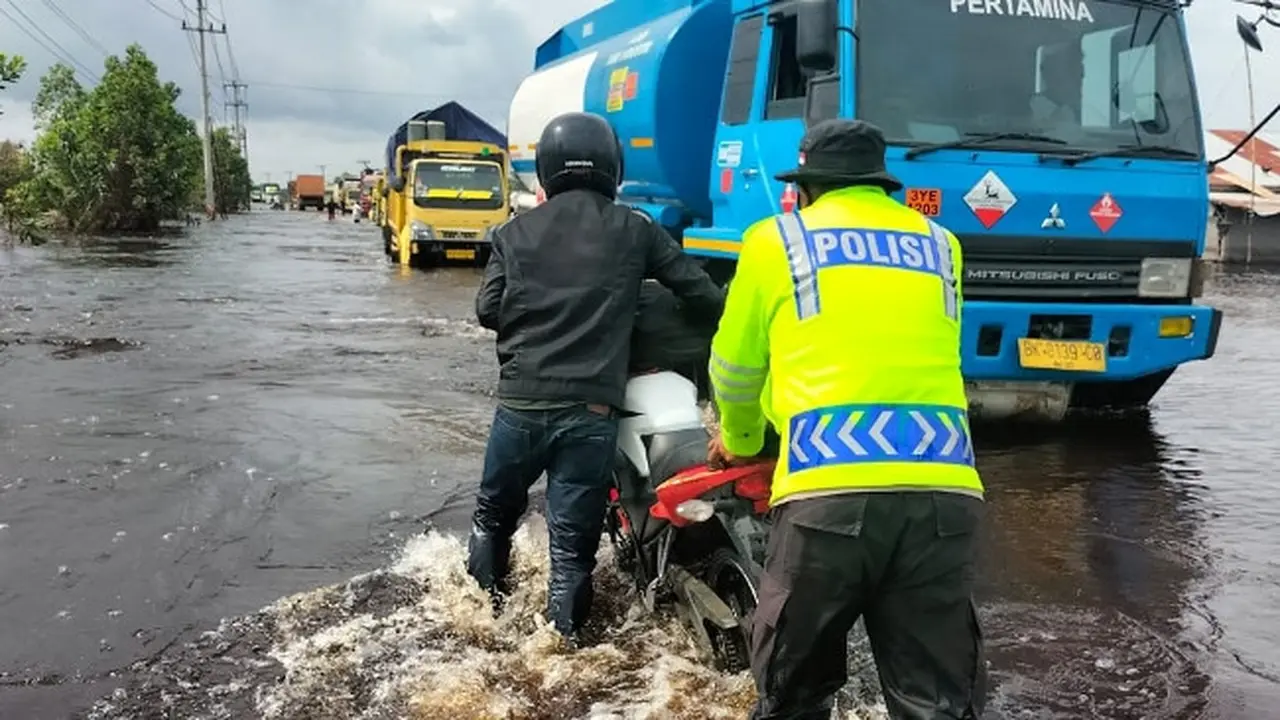 Personel Polres Pelalawan membantu mendorong sepeda mootor warga yang terjebak banjir.