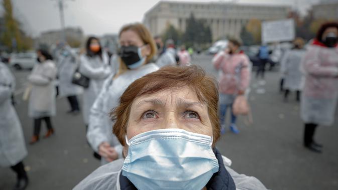 Seorang pekerja medis yang mengenakan masker melihat ke atas setelah melepaskan balon hitam di Bucharest, Rumania, Selasa (17/11/2020). Aksi tersebut untuk mengenang pasien COVID-19 yang tewas dalam kebakaran di IGD  sakit di Piatra Neamt, Rumania pada 14 November 2020 lalu. (AP Photo/Vadim Ghirda)
