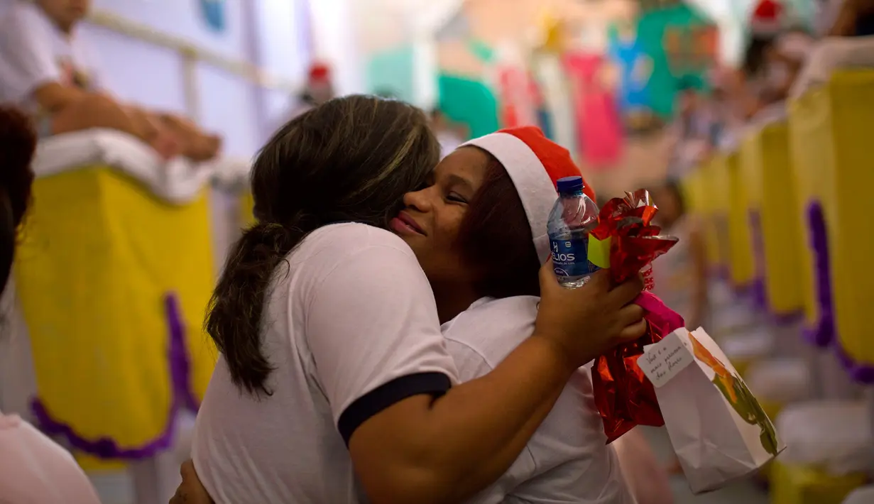 Narapidana perempuan (kanan) memeluk seorang sukarelawan dalam acara tahunan menghias sel menggunakan dekorasi bernuansa natal di Penjara Nelson Hungria, Rio de Janeiro, Kamis (13/12). (AP/Silvia Izquierdo)