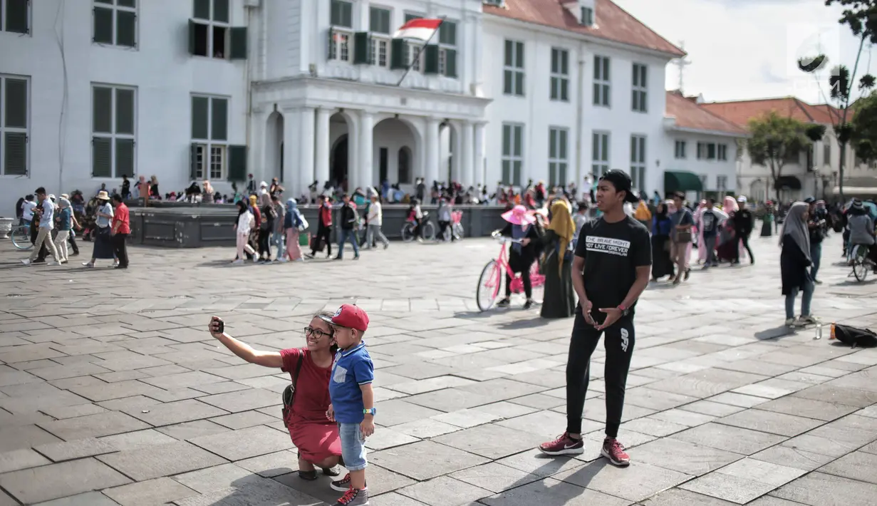 Pengunjung foto di depan Museum Sejarah Kota Tua, Jakarta, Kamis (27/12). Kawasan wisata Kota Tua dipadati wisatawan dari dalam kota maupun luar kota Jakarta selama libur sekolah. (Liputan6.com/Faizal Fanani)