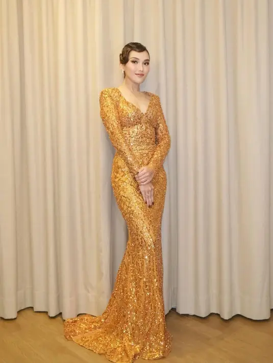 Ayu Ting Ting tampil memesona dibalut gaun emas. Gaun ini memiliki lengan panjang, detail garis leher yang dalam dan train panjang yang menjuntai hingga ke lantai. [Foto: Instagram/ayutingting92]