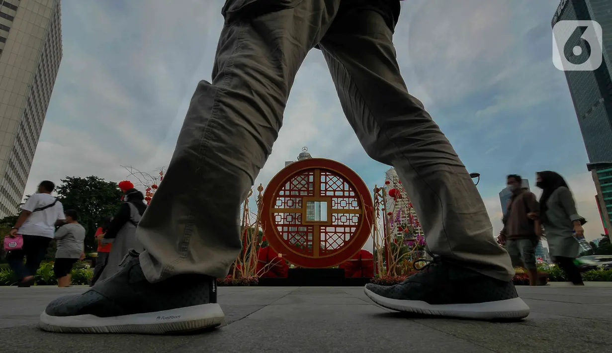 Pejalan kaki melintasi ornamen dengan nuansa Imlek di kawasan Bundaran HI, Jakarta, Sabtu (29/1/2022). Ornamen yang didominasi warna merah dan emas ini dipasang dalam rangka menyambut perayaan Tahun Baru Imlek 2573, yang jatuh pada 1 Februari mendatang. (Liputan6.com/Herman Zakharia)