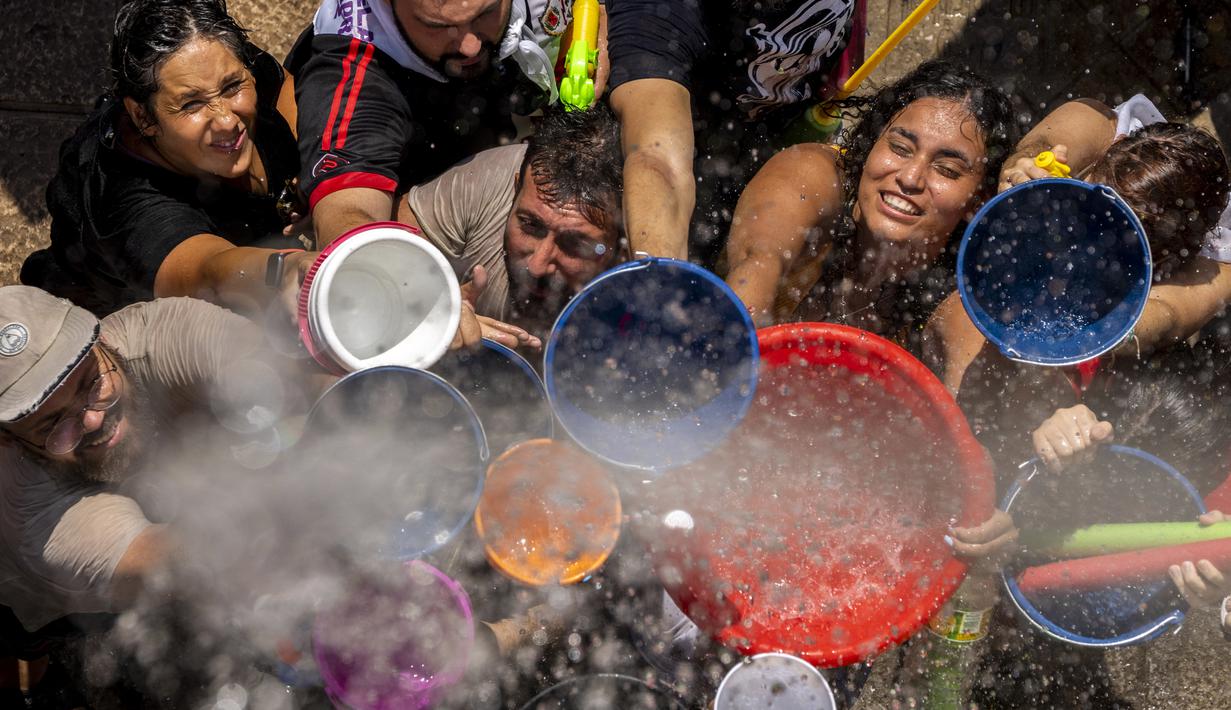 Orang-orang mengisi ember dan mangkuk mereka saat perang air tahunan di jalan-jalan lingkungan Vallecas, Madrid, Spanyol, 17 Juli 2022. Senjata yang diizinkan dalam acara ini adalah pistol dan ember air. (AP Photo/Manu Fernandez)
