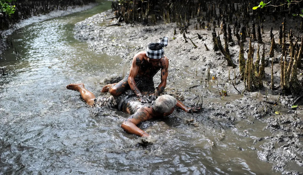 Seorang pria Bali bermain lumpur bersama temannya selama tradisi mandi lumpur atau dikenal sebagai Mebuug-buugan di desa Kedonganan, Denpasar, Bali (10/3). Mebuug-buugan diadakan sehari usai hari raya Nyepi. (AFP/Sonny Tumbelaka)