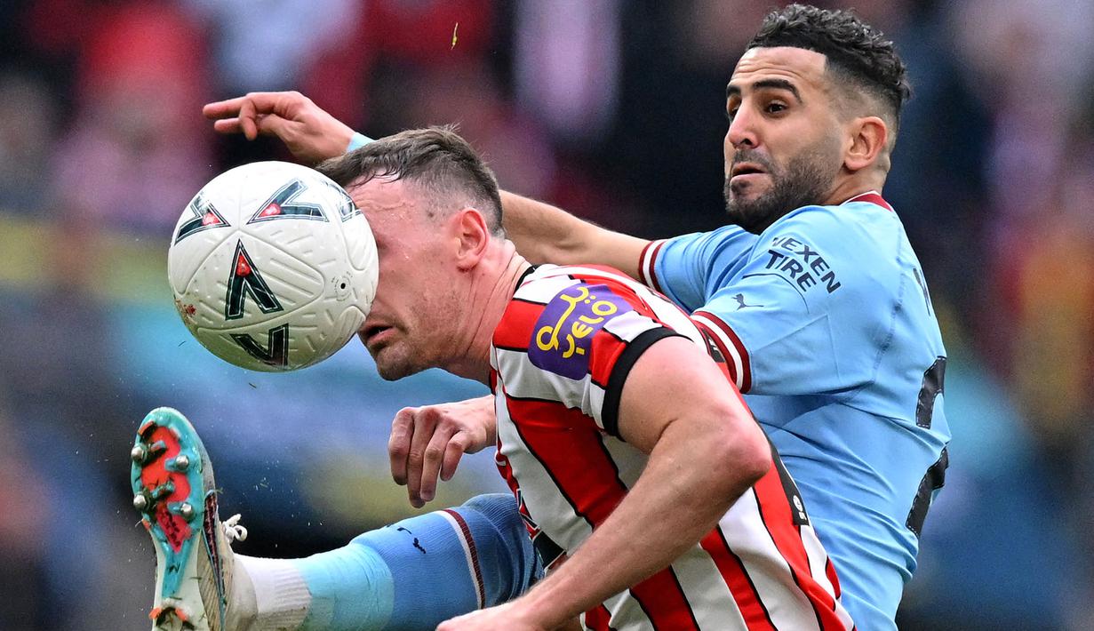 <p>Pemain Manchester City, Riyad Mahrez (kanan) berebut bola dengan pemain Sheffield United, Jack Robinson pada laga semifinal Piala FA 2022/2023 di Stadion Wembley, London, Minggu (23/04/2023) WIB. The Cityzens sukses meraih kemenangan melalui hattrick Mahrez. (AFP/Glyn Kirk)</p>