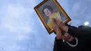 Seorang pelayat memegang potret Ratu Sirikit setelah iring-iringan mobil di Bangkok, Thailand pada Minggu 26 Oktober 2025. Persemayaman Ratu Sirikit berlangsung selama setahun dimulai pada 26 Oktober 2025 di Grand Palace, Bangkok, Thailand, setelah beliau meninggal dunia pada 24 Oktober 2025. (Chanakarn Laosarakham/AFP)