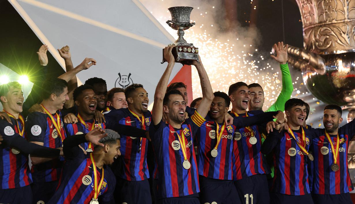 Kapten tim Barcelona, Sergio Busquet mengangkat trofi Supercopa de Espana 2023 disaksikan pemain lainnya setelah mengalahkan Real Madrid 3-1 dalam pertandingan Supercopa de Espana di King Fahd Stadium, Arab Saudi, Senin (16/1/2023) WIB. (AFP/Guiseppe Cacace)
