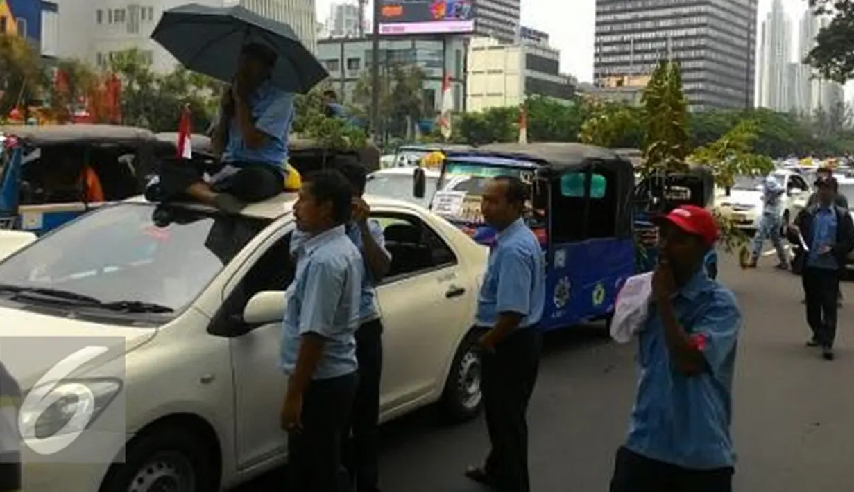 Sopir duduk diatas taksi membawa payung saat demo di depan Gedung DPR/MPR, Jakarta, Selasa (22/3). Selain melakukan demo, sopir taksi tersebut melakukan sweeping ke supir taksi yang beroperasi di dalam tol dan membakar ban. (Liputan6.com/Ahmad Romadoni)