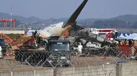 Petugas pemadam kebakaran dan petugas penyelamat bekerja di dekat reruntuhan pesawat Jeju Air Boeing 737-800 di Bandara Internasional Muan di Provinsi Jeolla Selatan, sekitar 288 kilometer sebelah barat daya Seoul pada tanggal 29 Desember 2024. (JUNG YEON-JE/AFP)