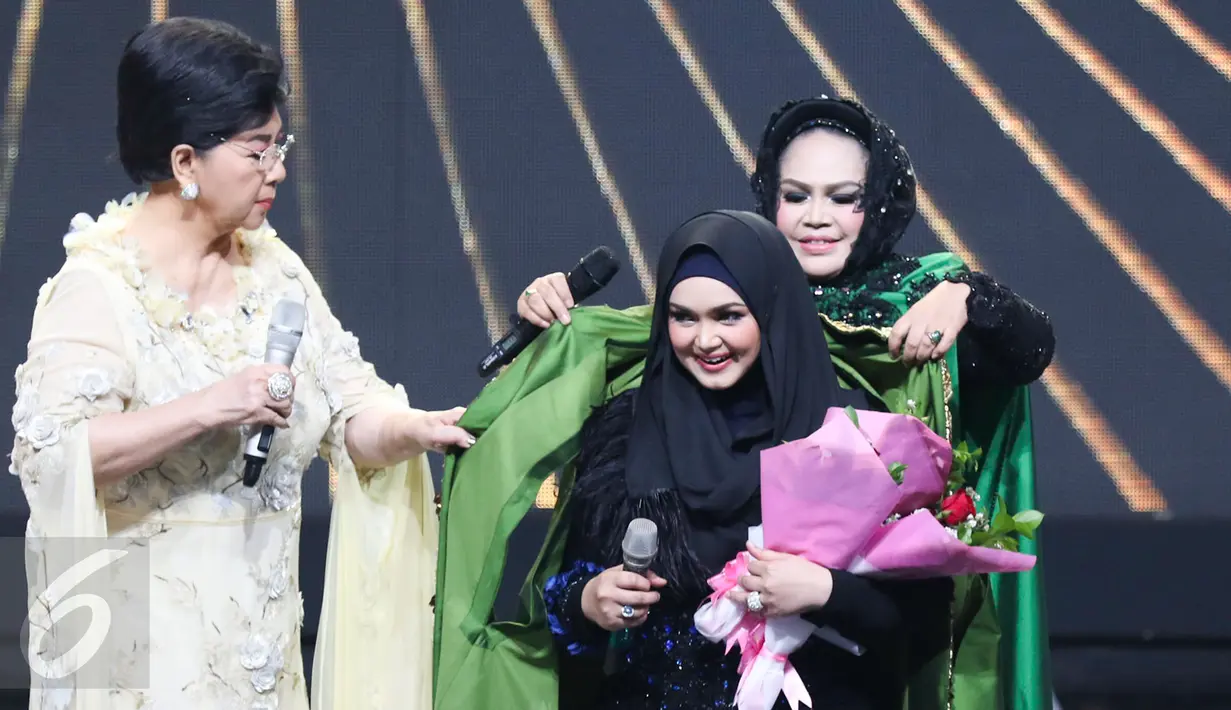 Hetty Koes Endang memakaikan kain hadiah ulang tahun untuk Siti Nurhaliza dalam acara Golden Memories International di Indosiar, Jakarta, Kamis (12/1). (Liputan6.com/Yoppy Renato)