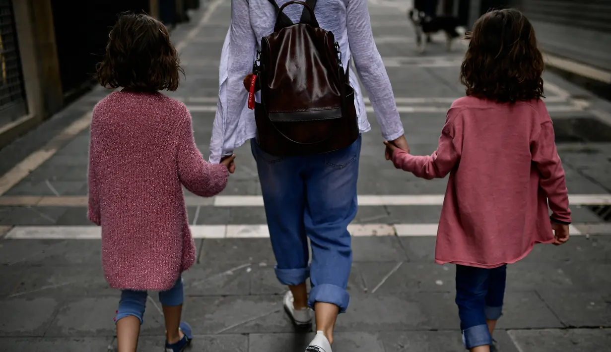 Keluarga berjalan-jalan di sepanjang jalan kota lama, di Pamplona, Spanyol utara (27/4/2020). Anak-anak di bawah 14 tahun diizinkan untuk berjalan-jalan dengan orang tua hingga satu jam dan dalam satu kilometer dari rumah, mengakhiri enam minggu pembatasaan. (AP Photo/Alvaro Barrientos)
