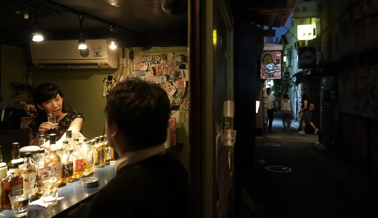 Pemilik bar Marie Yoshida (kiri) mengobrol dengan pengunjung di barnya di Golden Gai di distrik Shinjuku Tokyo (28/7/2019). Lebih dari 200 bar kecil bergaya klub dan restoran di area ini. (AP Photo / Jae C. Hong)