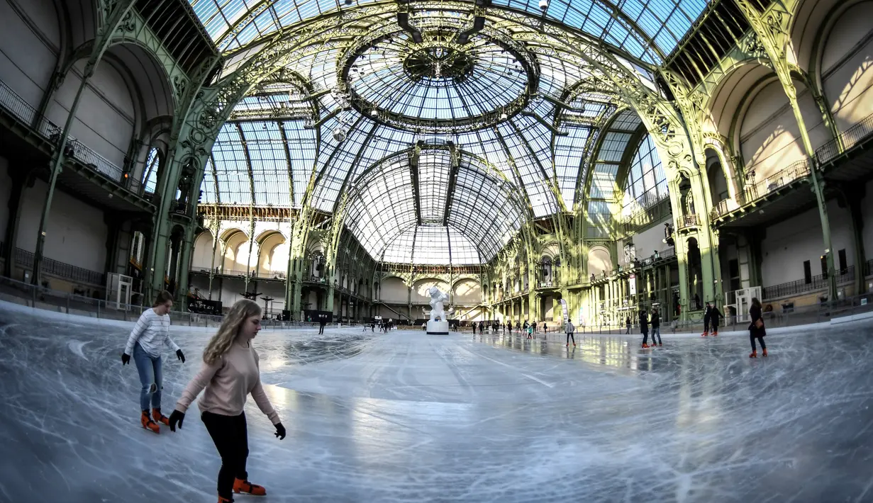 Orang-orang  berseluncur di arena ice skating di bawah kubah kaca mewah legendaris, Grand Palais, Paris, Senin (17/12). Arena ice skating musiman ini terbuka untuk umum selama liburan Natal. (STEPHANE DE SAKUTIN / AFP)