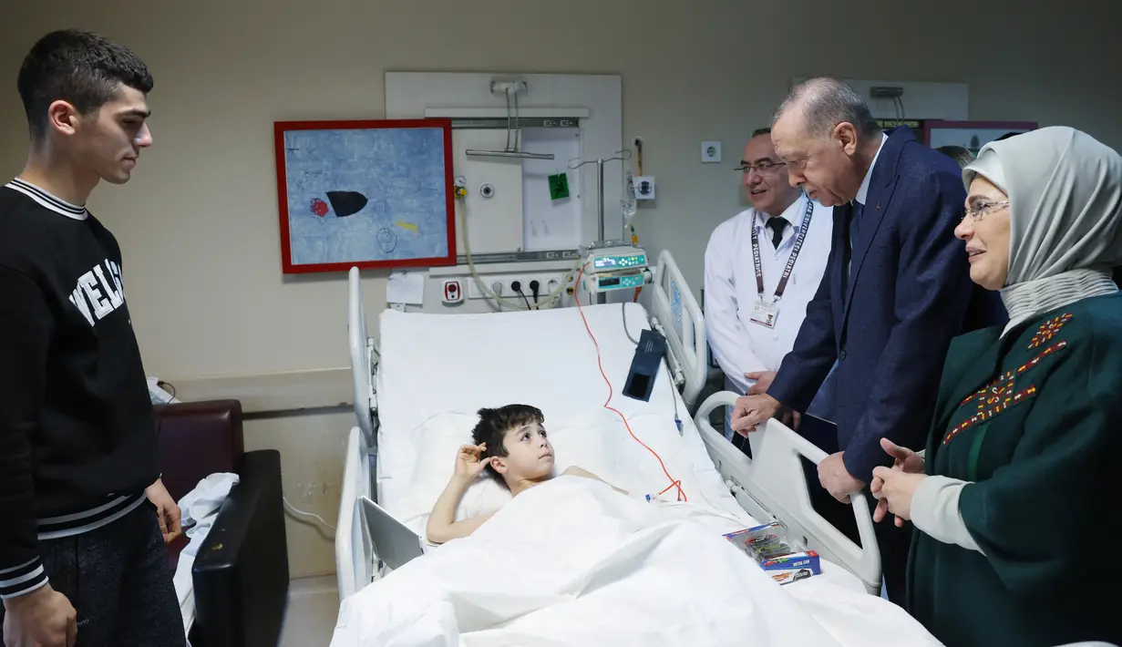 Gambar selebaran yang dirilis pada 22 Februari 2023 menunjukkan Presiden Turki Recep Tayyip Erdogan (kedua kanan) dan istrinya Emine Erdogan mengunjungi anak korban gempa yang menerima perawatan di Fakultas Kedokteran Universitas Ankara setelah dipindahkan dari daerah yang dilanda gempa di Turki. Presiden Erdogan menjanjikan akan menghidupkan kembali daerah terdampak gempa Turki dalam jangka waktu setahun. (Press Office of the Presidency of Turkey / AFP)