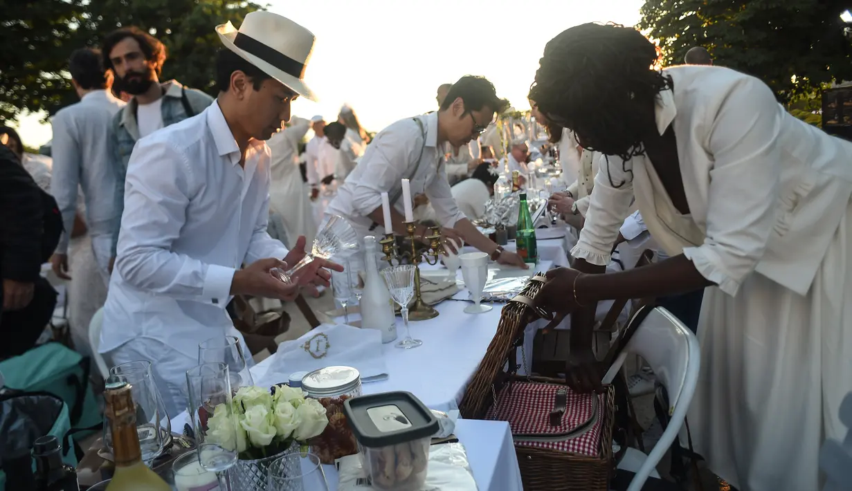 Para peserta dalam balutan serba putih  berkumpul untuk Dinner en Blanc atau "makan malam putih" di Tuileries Gardens, Paris, Kamis (6/6/2019). Saat acara, baik pria maupun wanita tampil gaya dengan topi mewah, mantilla, bulu dan gaun berenda. (Lucas BARIOULET/AFP)