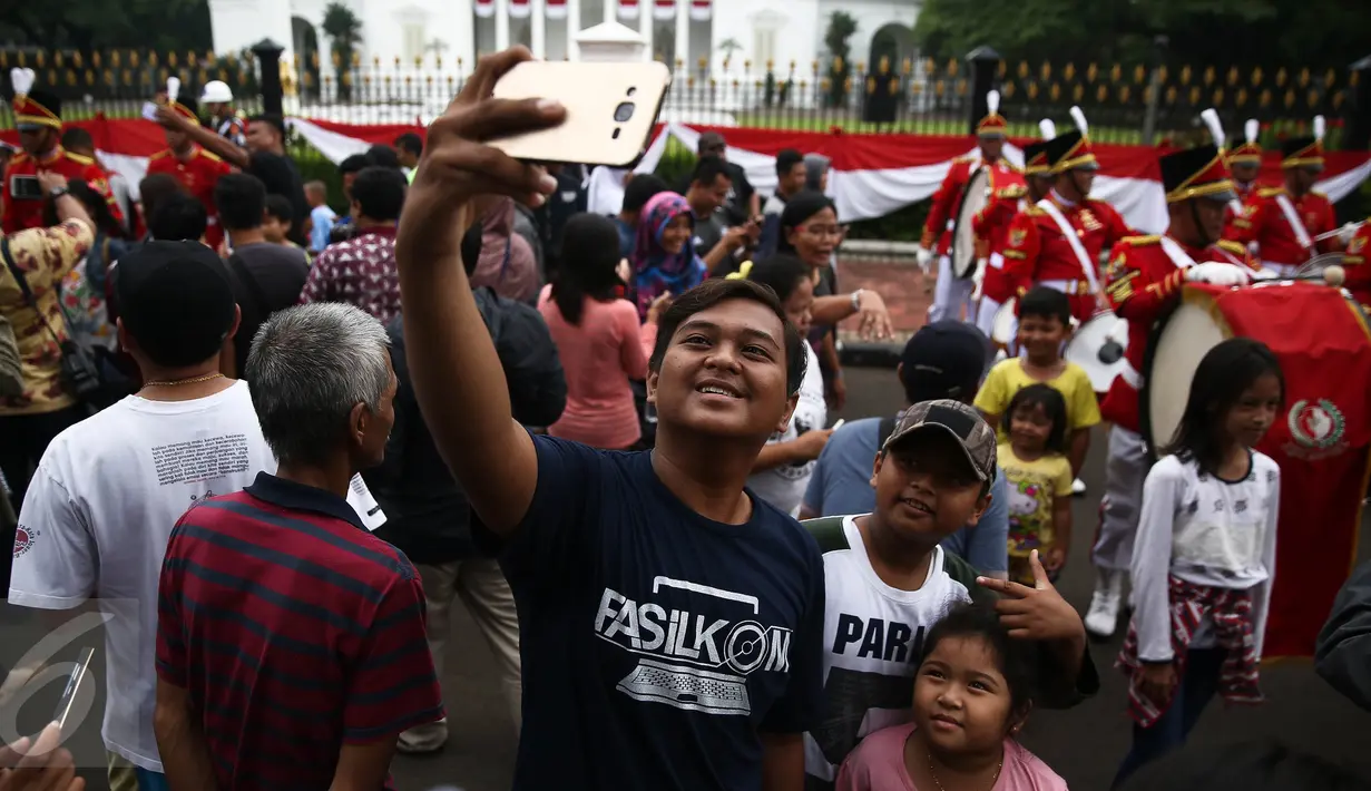 Warga berfoto dengan latar belakang anggota Paspampres yang melakukan prosesi pergantian jaga Istana Kepresiden di depan Istana Merdeka, Minggu (28/8). Seremoni pergantian pasukan ini mengundang perhatian warga. (Liputan6.com/Faizal Fanani)