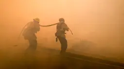 Dua petugas pemadam kebakaran berusaha memadamkan api di sepanjang Ronald Reagan (118) Jalan Bebas Hambatan di Simi Valley, Californnia (12/11). Kebakaran yang terjadi dilaporkan telah menewaskan puluhan orang. (AP Photo / Ringo H.W. Chiu)