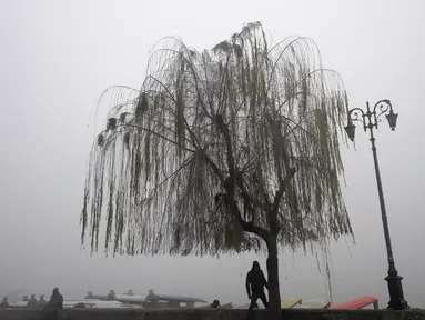 Seorang pria Kashmir berdiri di bawah pohon willow sambil menunggu pelanggan menaiki shikara, gondola perahu dayung tradisional, di tepi Danau Dal pada suatu pagi yang dingin dan berkabut di Srinagar, Kashmir yang dikuasai India, Jumat, 29 Desember. 2023. (AP Photo/Dar Yasin)