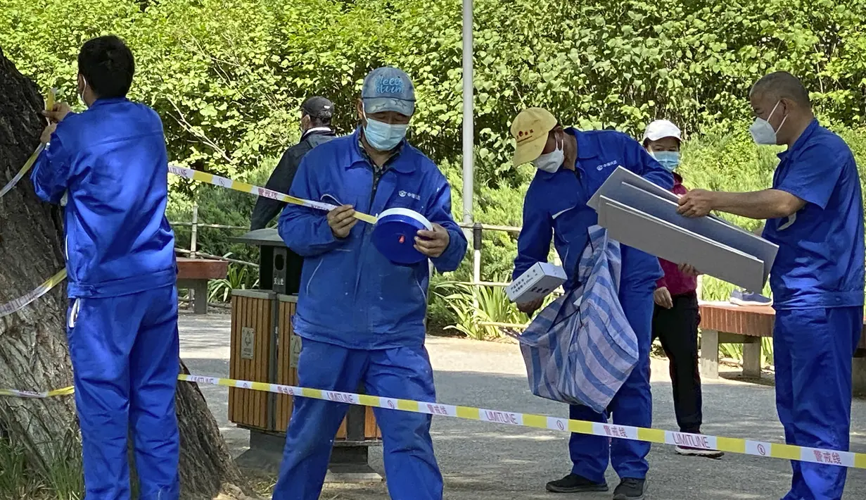 Pekerja memasang garis peringatan untuk menutup sebagian ruang hijau di sepanjang jalur air di Beijing, China, Selasa (17/5/2022). Pada Minggu (15/5) kemarin, Beijing memperpanjang aturan untuk bekerja dari rumah di empat distrik. Itu sudah melarang layanan makan di restoran dan membatasi transportasi umum, di antara langkah-langkah lainnya. (AP Photo/Mark Schiefelbein)