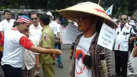Cak Tatang namanya. Dia berdiri di halaman gedung Mahkamah Konstitusi (MK), Jakarta dengan topi caping ala petani. (Ahmad Romadoni/Liputan6.com)