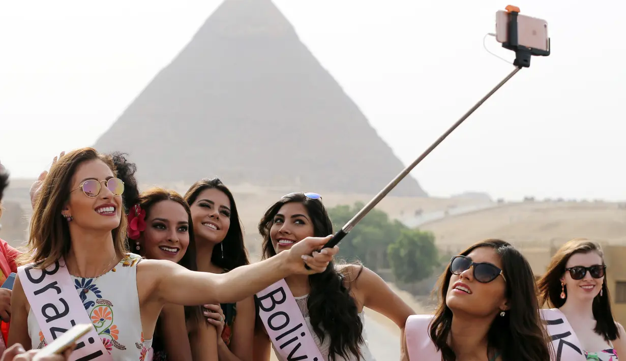 Kontestan Miss ECO Universe berselfie menggunakan tongsis dengan latar belakang segitiga piramida di pinggiran Kairo, Mesir (10/4). Pemenang Miss Eco Universe 2016 akan memenangkan hadiah uang tunai USD 10.000. (REUTERS/Mohamed Abd El Ghany)