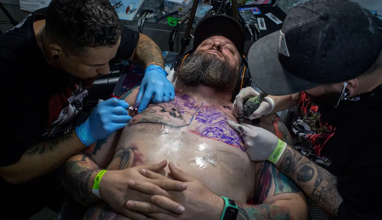 Dua seniman tato sedang berkarya di tubuh seorang pria saat acara Tattoo Week tahunan di Rio de Janeiro, Brasil (12/1). Ajang perhelatan seniman dan penggemar tato ini diadakan setiap tahunnya di Brasil. (AFP Photo/Mauro Pimentel)